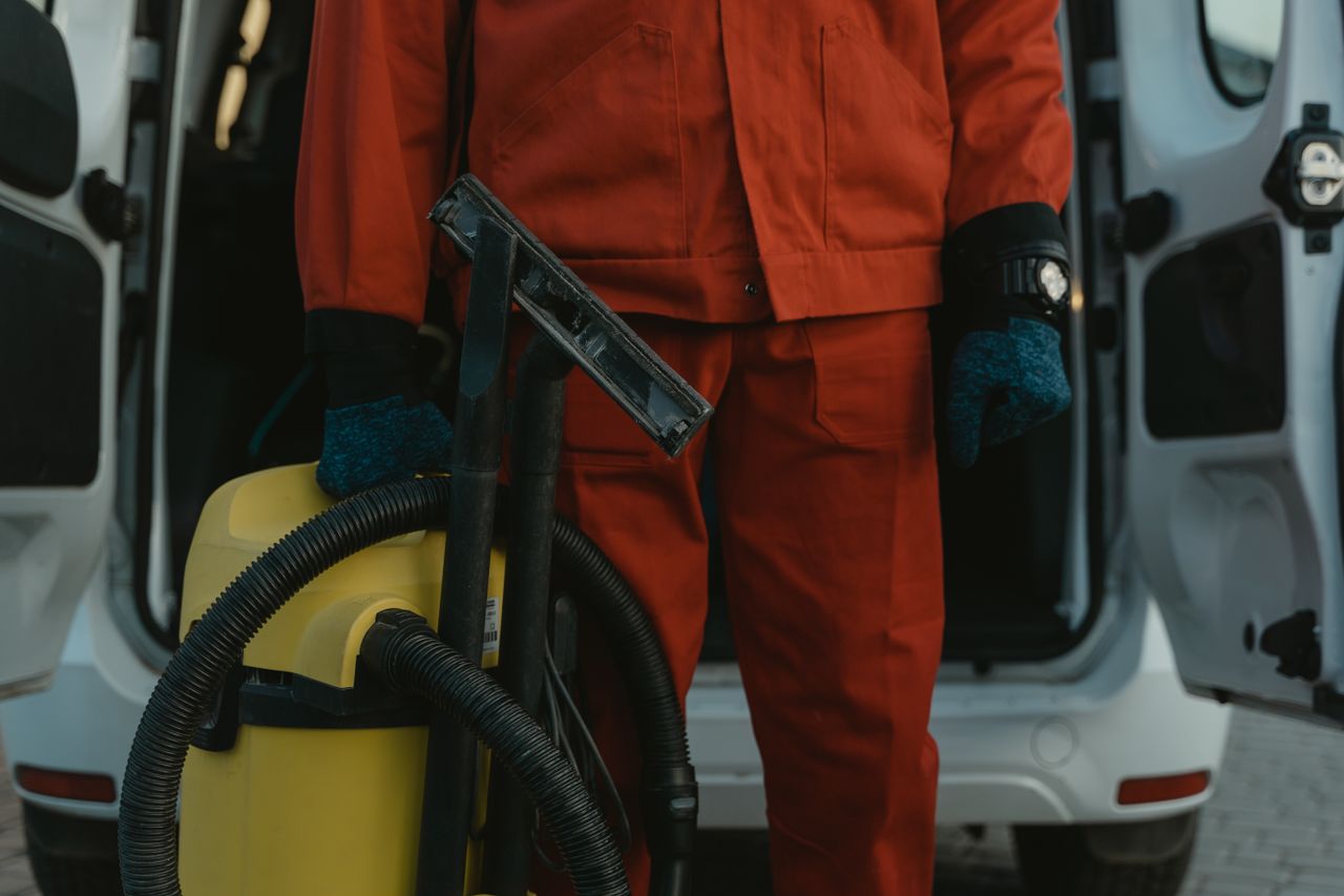 Un agent d’entretien professionnel en uniforme rouge, aspirateur à la main près d’un van, prêt à intervenir.